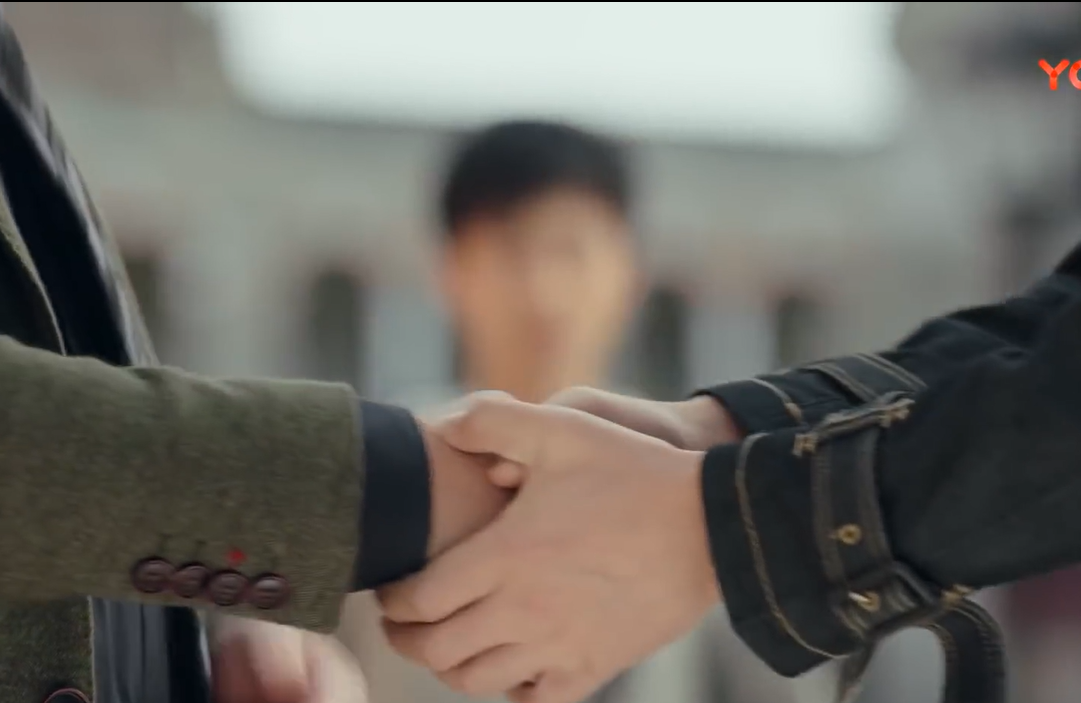 Two hands clasped with an unfocused view of Guo Changcheng's face.